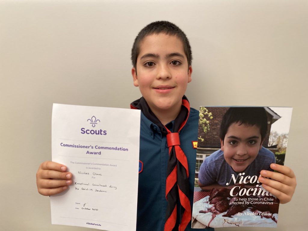 Nicolas Olmos, a Scout, holding his award and the cookbook he made to raise money.
