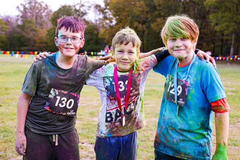 Three Scouts covered in mud and paint at the finish line of the race with medals.
