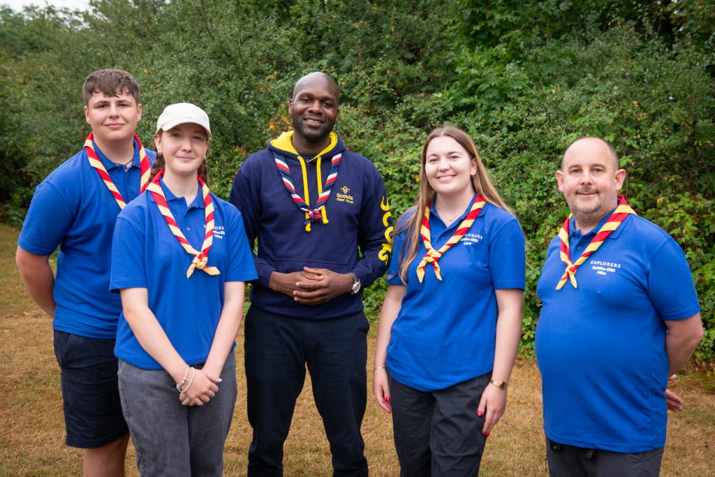 Five people stand for a photograph wearing Scout neckers and activity clothing. Left to right they are Charlie Prior-Turner, Explorer Scout, Libby Roy, Explorer Scout, Dwayne Fields, Chief Scout, Chloe Knott, Explorer Scout, and Mike Baxter, Lead volunteer for Top Awards in Hampshire.