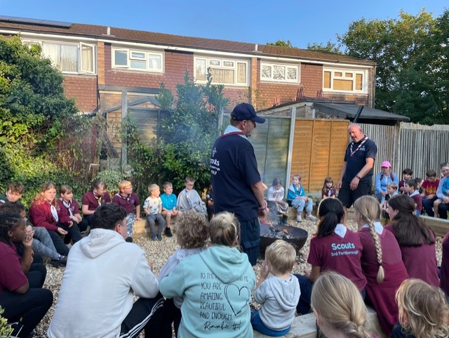 Around thirty young people enjoy a campfire with two leaders standing around the fire leading songs.